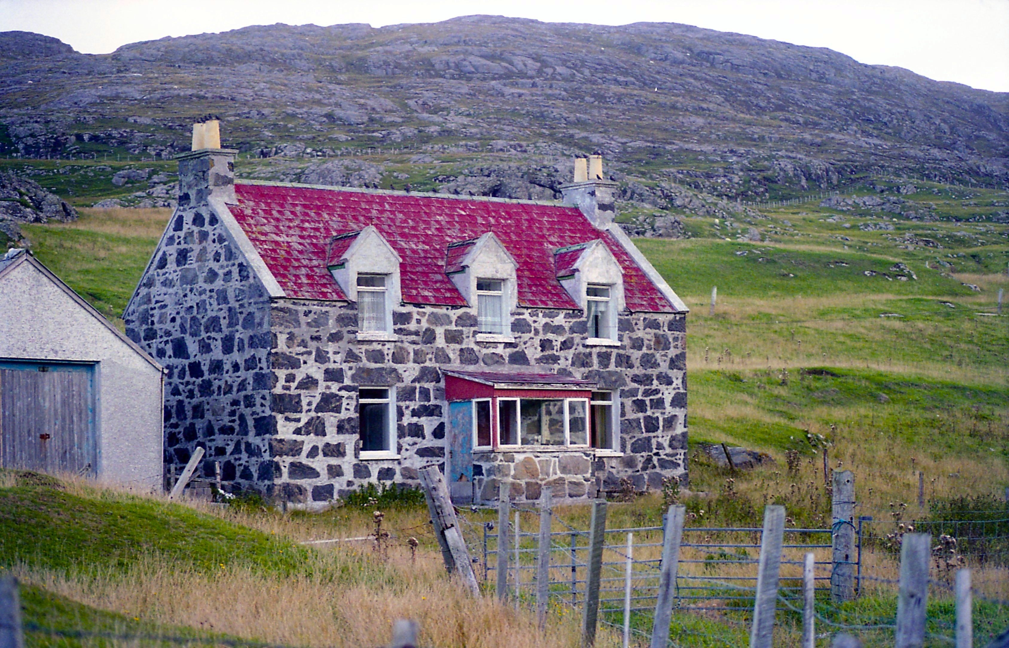 Image of a croft house in front of a hill in rural Scotland.